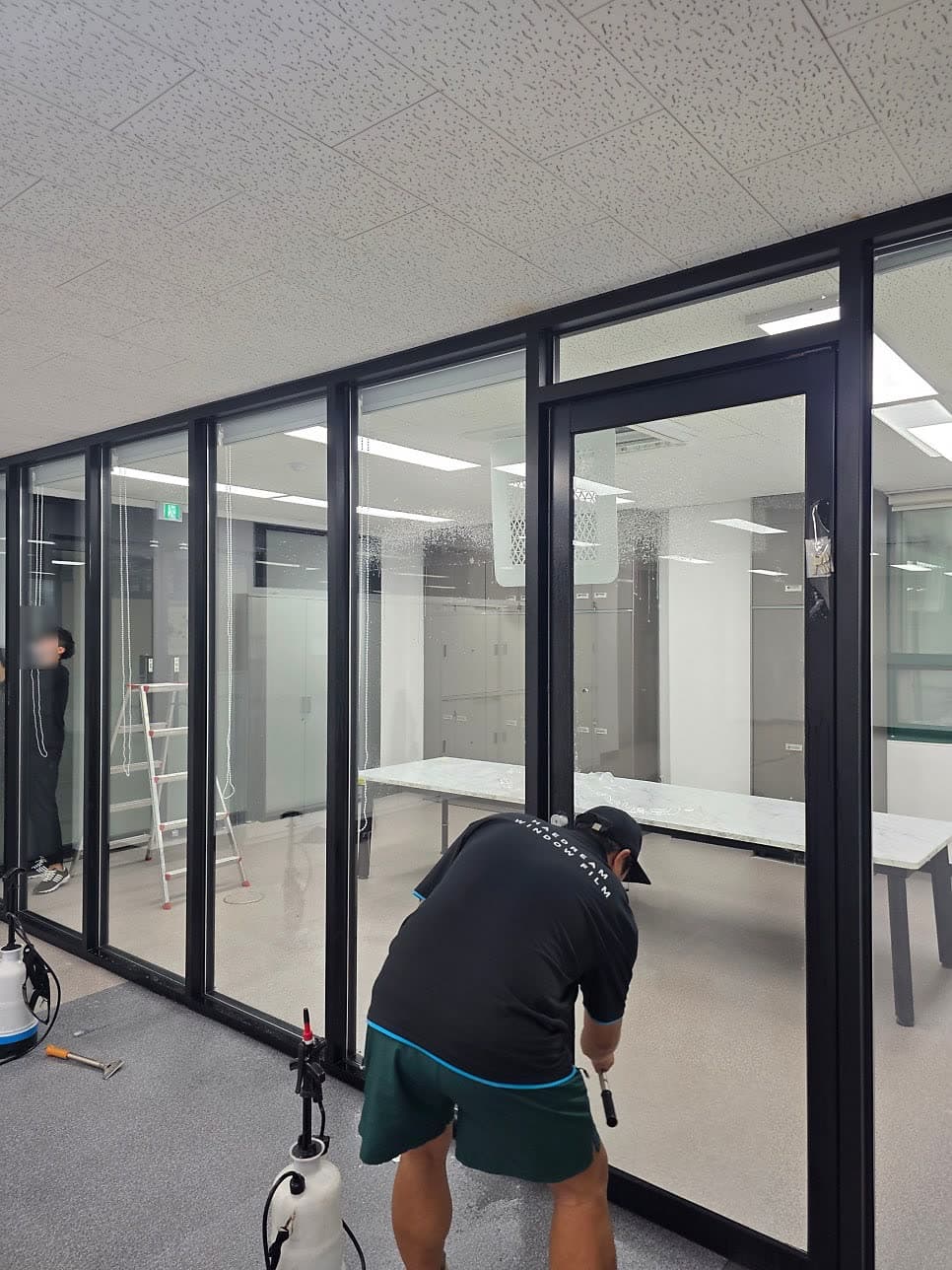 해드림 시공자가 사무실 유리 파티션에 필름을 시공하는 모습